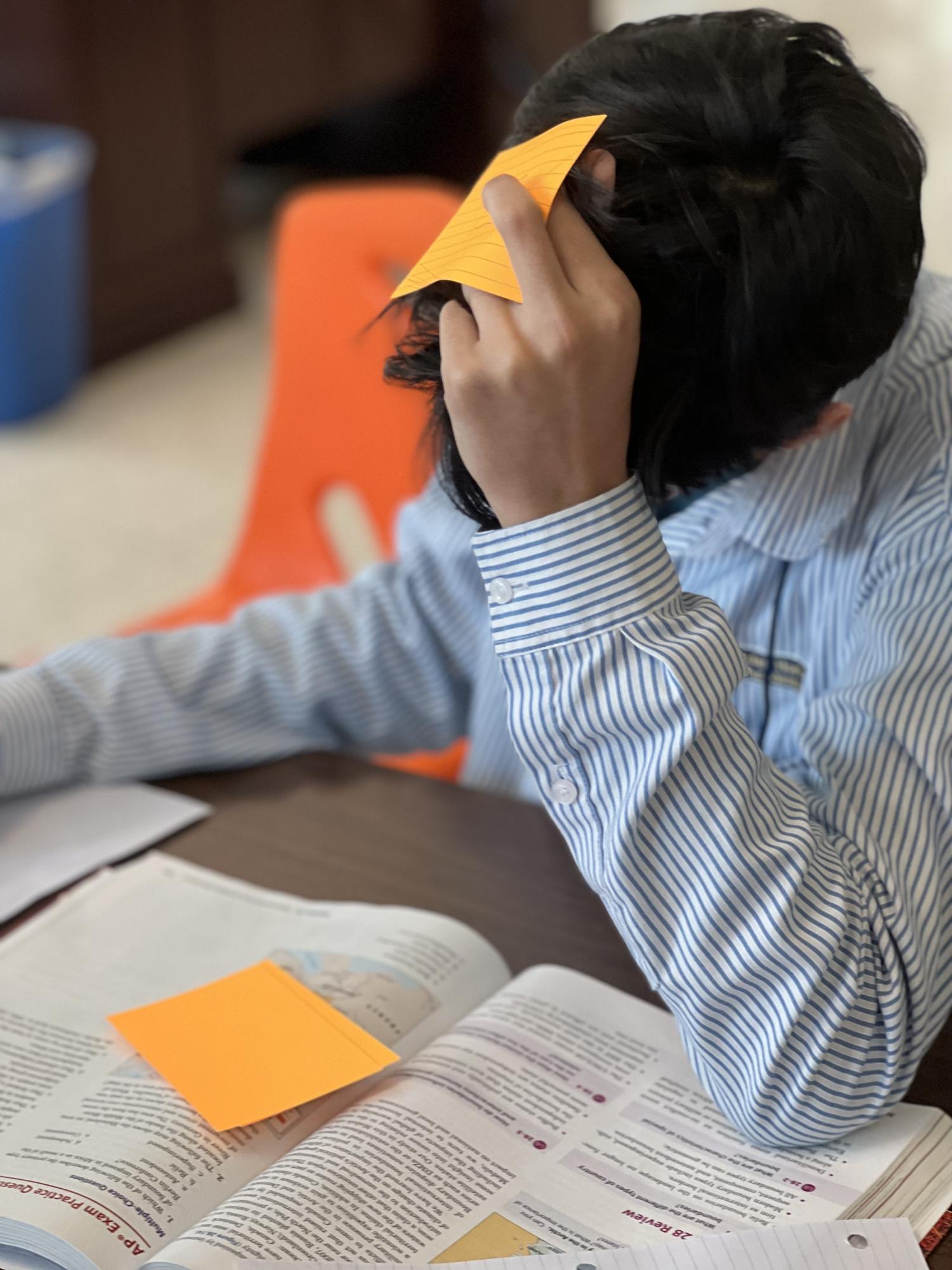 Freshman, Sulaiman Mohammed, deeply focused and showing signs of concentration, completes a homework assignment during lunch in the library. This moment captures the pressures of academic workload as he works to finish tasks from the previous night.