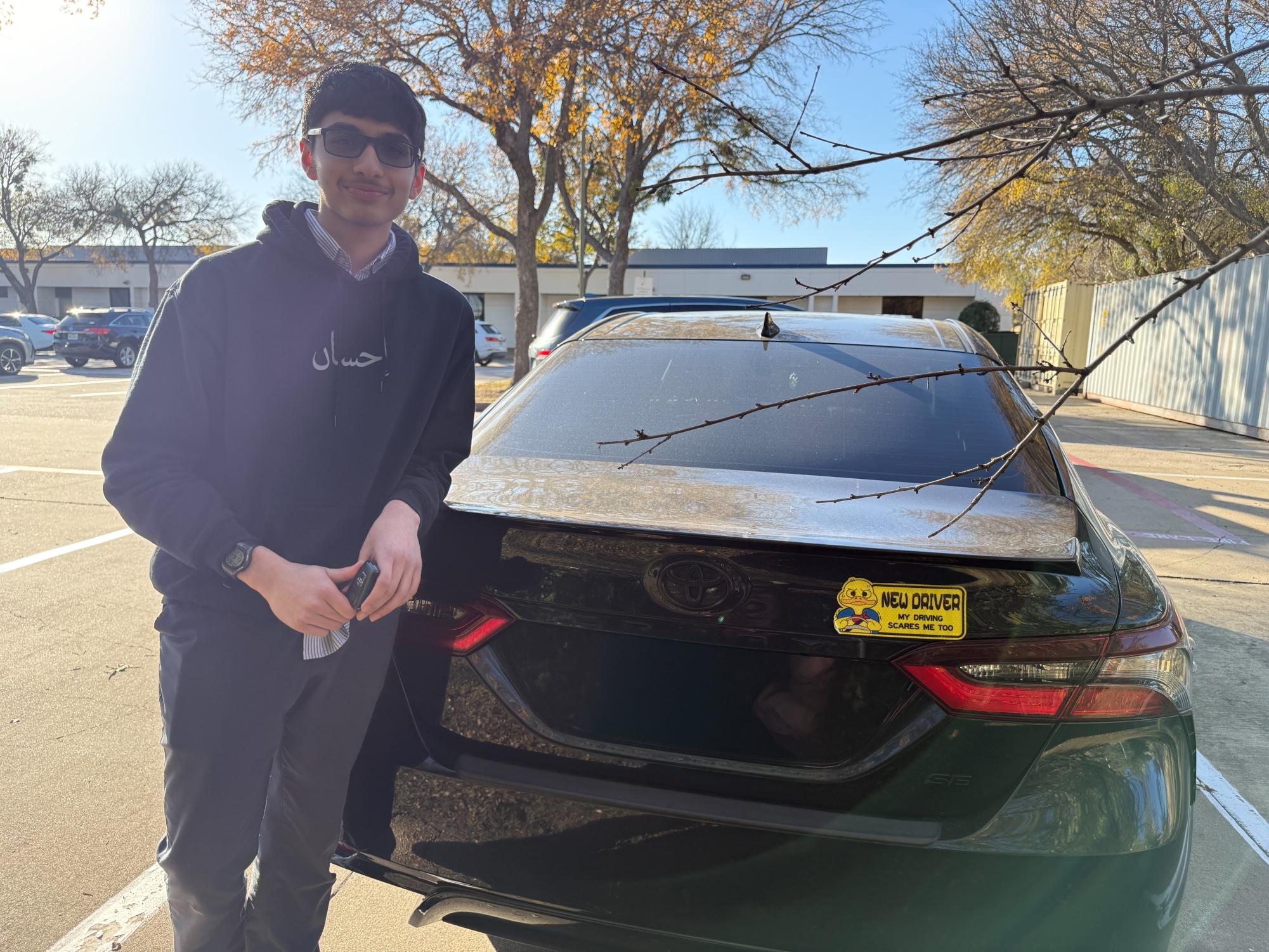 Junior Osayd Haq stands beside his Toyota Camry, with a "New Driver" sticker on the back. (License plate obscured for privacy)
